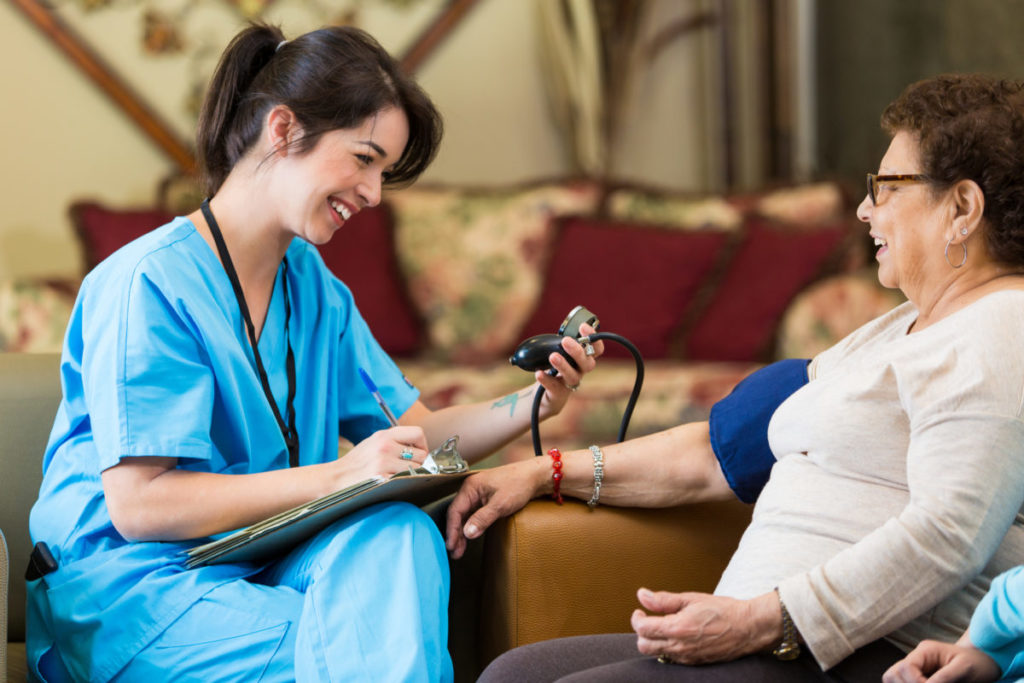Home healthcare nurse checks senior female patent's blood pressure during home visit. The nurse writes down the patient's blood pressure reading on the patient chart