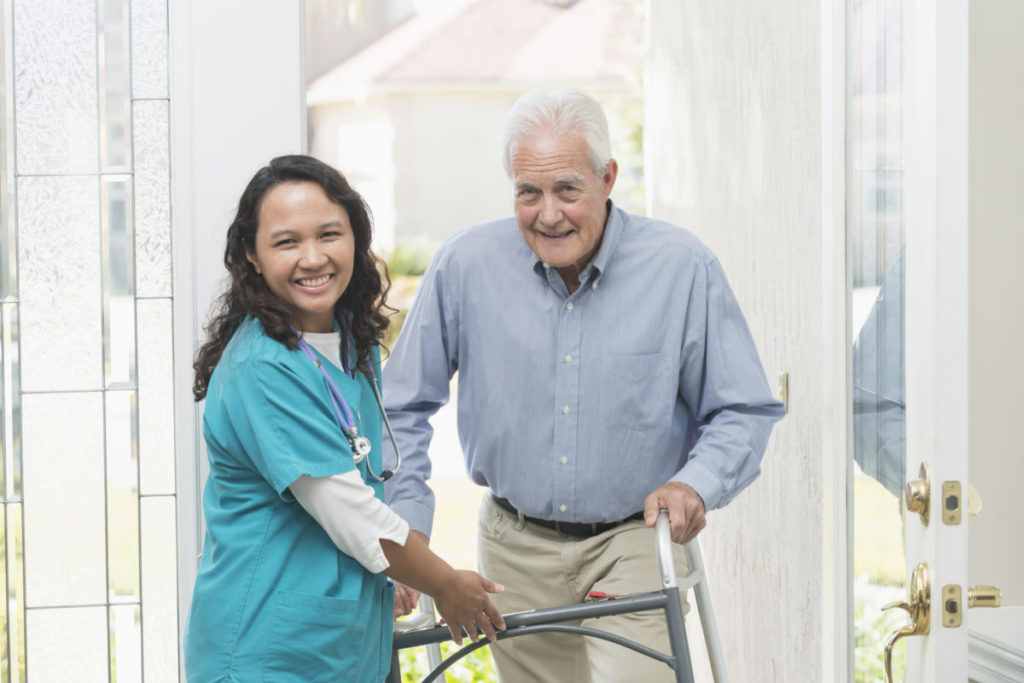 Home healthcare worker helping elderly man with walker