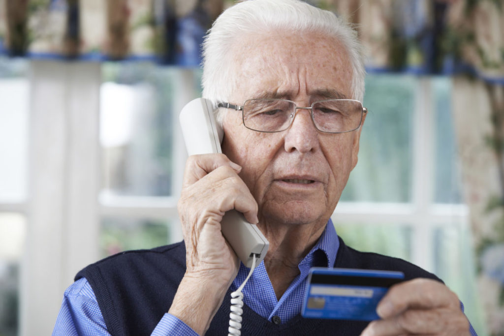 Male Caucasian senior looking at credit card while talking on the phone
