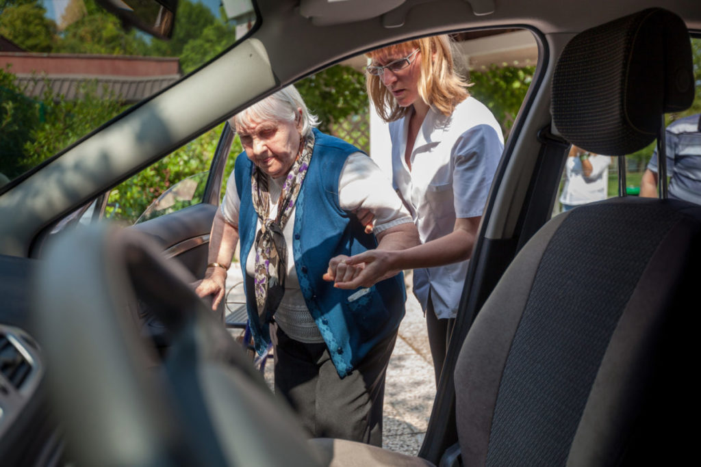 Personal Assistant Helping to Senior Woman into Car