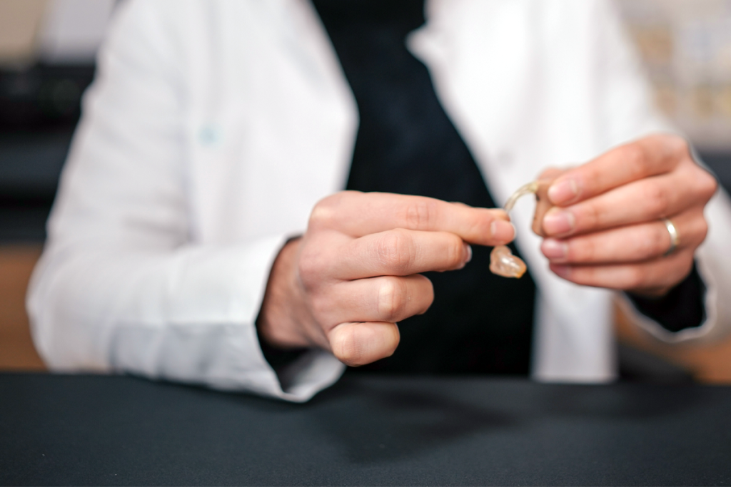 A person in a white coat holding a hearing aid
