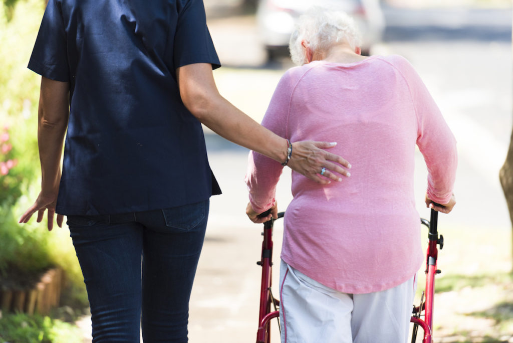 Caregiver helping an elderly woman with her walking aid outdoors in the grounds of the retirement home