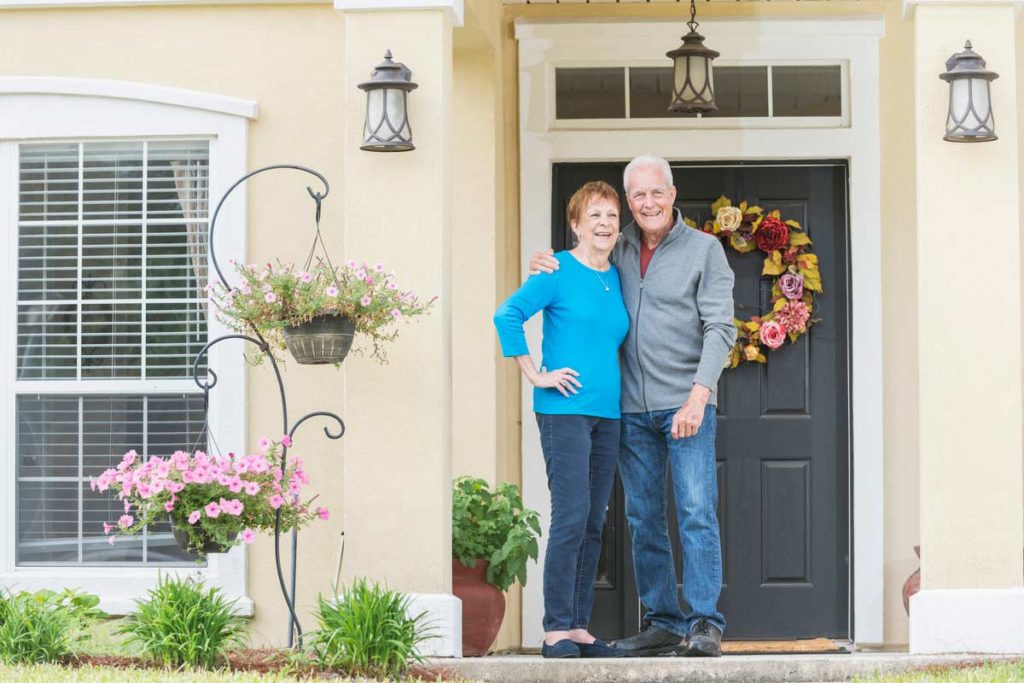 elderly couple standing in front of home