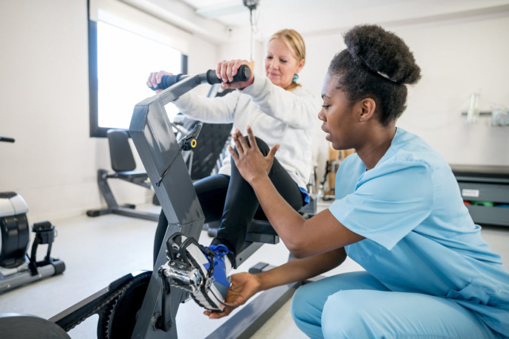 alt="African american occupational therapist explaining a patient how to use the static bicycle"