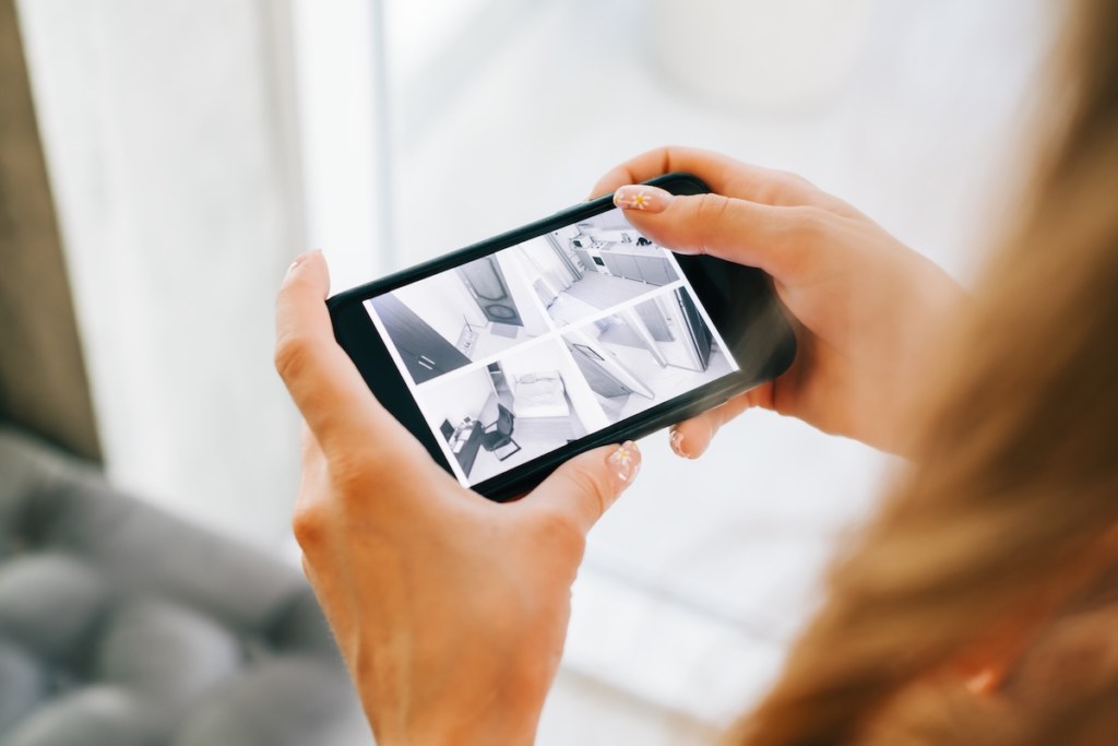 Caucasian woman monitoring security cameras on smartphone indoors, closeup.