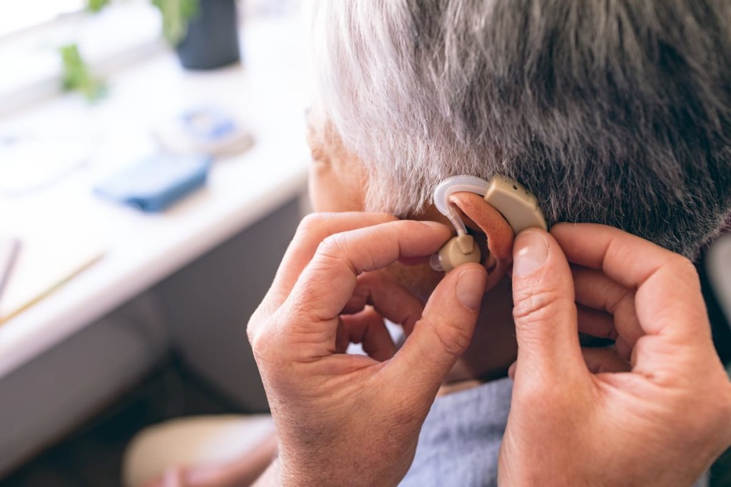 male doctor applying hearing-aid to senior woman